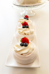 Delicious meringue dessert topped with whipped cream, strawberries, and blueberries on a white platter.
