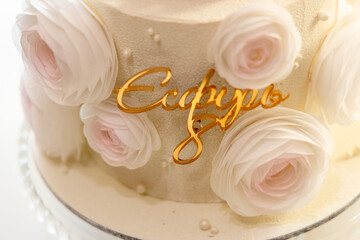 An elegant cake adorned with delicate white and blush roses, featuring a golden, stylish inscription that reads 'Есфирь' in the center.