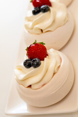 Delicious mini pavlova desserts topped with whipped cream, fresh strawberries, and blueberries.