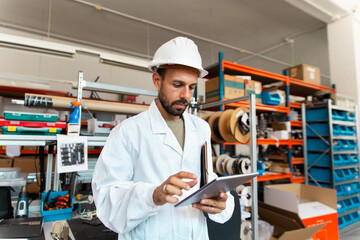 Lab technician with protective helmet using tablet in electronics workshop