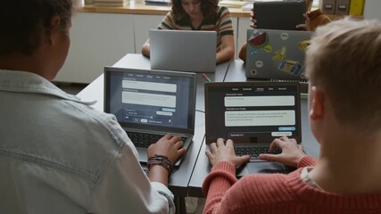 Medium rear shot of group of busy diverse young children sitting at desks in classroom at STEM lesson, writing prompts for AI image generator program on laptops, while working on projects - Powered by Adobe