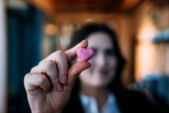 Businesswoman holding heart-shaped candy with positive gesture indoors