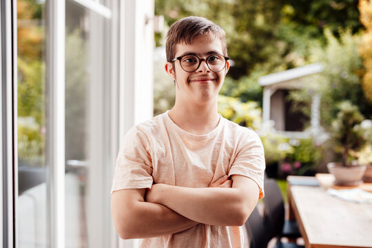 Teenager with trisomy 21 standing outdoors smiling with folded arms