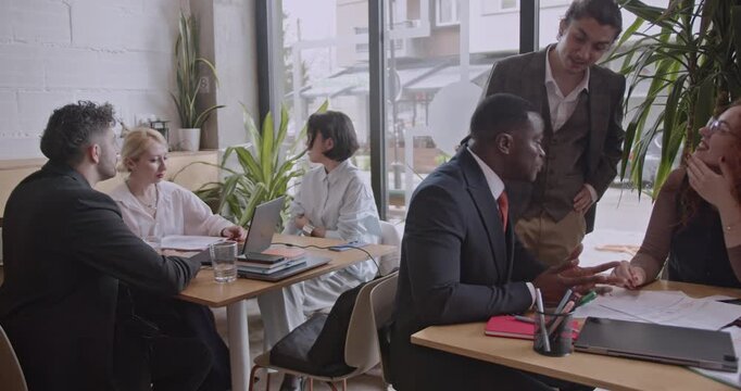 Diverse colleagues brainstorm and analyze data in a co working space coffee bar. International startup team discusses project strategy and plans.