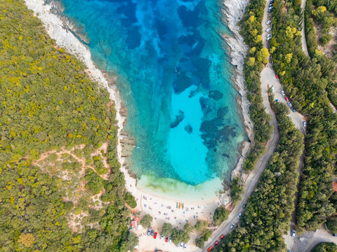 Aerial view of turquoise waters meeting the white sands of a secluded beach, embraced by verdant forests, creating a striking contrast of colors, Emblisi beach, Kefalonia, Greece.