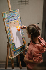 Child draw a picture in art class. Girl enjoys painting in a workshop. Art lesson. Education and learning concept. School kid drawing with brush landscapes on easel. Mix and combine colors.