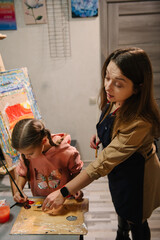 Artist explains how to mix and combine colors. Childs painting in workshop. Kids drawing brush on easel. Teacher learn children to draw pictures in an art lesson. Education, learning concept.