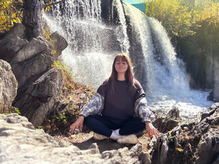 Caucasian woman meditates in nature near waterfall