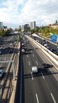 Vertical 4K video of heavy traffic on the eastern section of Madrid&rsquo;s M30 highway, filmed from a bridge facing north. Dense car congestion on central and service lanes under clear daylight.