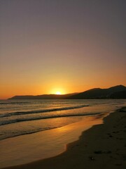 An evening sunset over the sea and beach with dramatic clouds reflects in the water near the coast