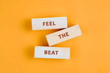 Three wooden blocks are stacked, each bearing a word feel, the, beat. They rest on an energetic orange surface, inspiring a sense of musicality and energy