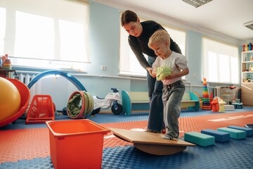 Balancing, walking. Preschool child with teacher during developmental activities in a playroom