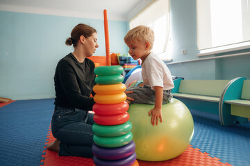 On the ball, putting rounded toys on the stick, balance. Preschool child with teacher during developmental activities in a playroom