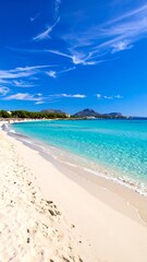 A long, sunny beach with white sand meets crystal-clear turquoise water. Blue sky has wispy clouds. A distant treeline is seen