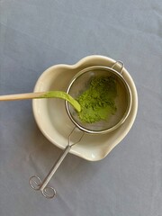 Bamboo spoon with matcha green tea powder over sieve. 