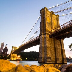 A long-exposure shot shows a majestic suspension bridge at dusk. Its towers glow, the sky a gradient of blue. Lights twinkle