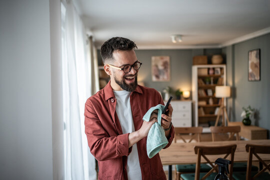 Happy man cleaning smartphone for hygiene at home - Powered by Adobe