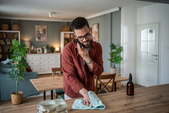 Man multitasking cleaning kitchen surface while talking on phone