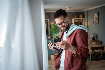 Fototapeta premium Smiling man using phone and holding vape device indoors