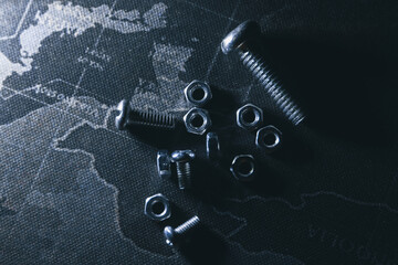 Dark abstract concept image of metal nuts and bolts scattered on global world map. monochrome and mysterious top view showing hardware, industry, and construction