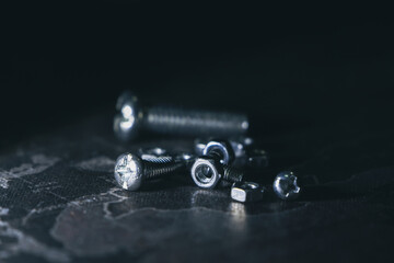 Dramatic macro close up of pile of metal nuts and bolts. Industrial steel hardware components, including screw and fastener, on dark black background with reflection