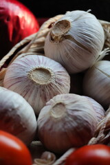 Garlic bulbs stored in a small woven wooden basket with tomatoes, rustic kitchen and organic food concept