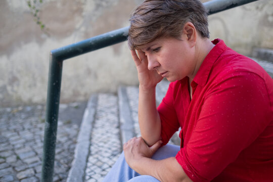 35 year old European woman sitting outdoors looking worried, thinking about life