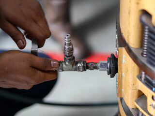A worker's hands connect a metal valve and fitting to heavy industrial machinery, illustrating a critical step in system assembly or maintenance.