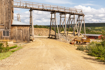 At Olav's Copper Mine, the Storwartz Mining Area features old wooden structures and mining machinery under a bright summer sky in R&oslash;ros Norway. The road leads through a historic mining site