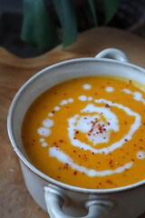 Autumnal pumpkin soup served with cream and chili flakes in a small pot, perfect food photography, cozy seasonal meal concept for thanksgiving