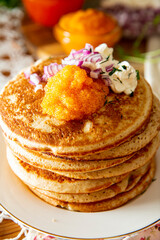 Rustic table setting with pancakes, caviar, sour cream, and onion - cozy homemade winter meal inspired by Nordic tradition.