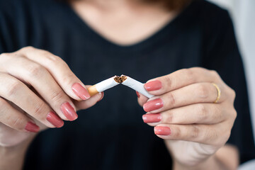 woman’s hand breaking a cigarette in half, symbolizing quitting smoking, health awareness, and...