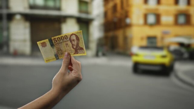 Hand holding hungarian forint banknote outdoors on city street with man in background showcasing urban economy and travel concept in vibrant street scene.