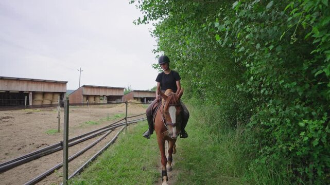 Female Rider Walking Horse Beside Green Hedge