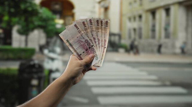 Man holding saudi riyal banknotes on a city street with buildings in the background reflecting urban financial outdoor theme