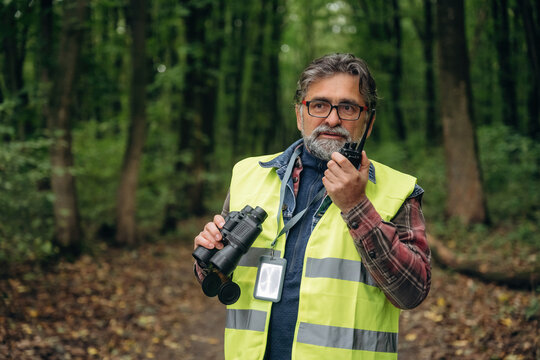 Talking by walkie talkie. Senior forest ecologist is working in the woods. In the uniform - Powered by Adobe