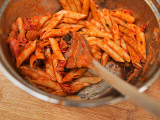 Metal pot with cooked pasta dish in red sauce with wooden spoon in it. Selective focus. Fine dinner serving. Food leftovers. Italian style dish.