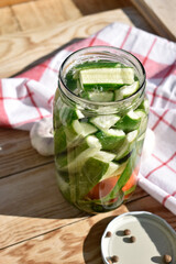 Pickled Cucumbers and Tomato with Herbs and Spices in Glass Jar on Wooden Table