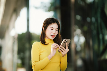 A young woman in a yellow sweater uses her smartphone outdoors, representing communication, social media, and modern digital lifestyle.