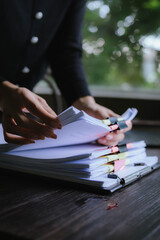 Businessperson organizing and reviewing stacks of paper documents and reports on a wooden desk in an office environment.