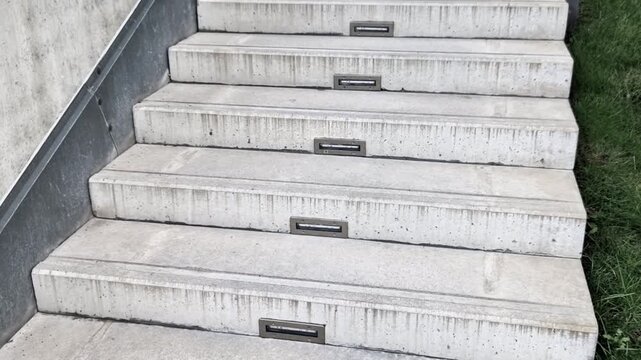 gray monolithic concrete park bench made of concrete in the shape of round stones wooden staircase bench with staircase lighting with metal railing black lattice on the stairs, wheelchair ramp