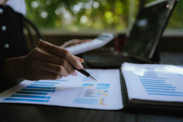 Businesswoman analyzing financial data using calculator, holding documents surrounded by charts, graphs and laptop, showing professionalism, business planning.