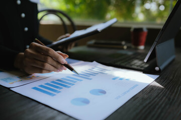 Business person analyzing financial charts and graphs on paper with a pen, working on data and...
