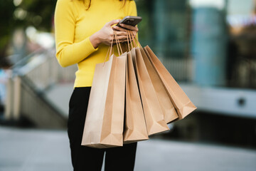 A person wearing a yellow sweater holds several brown paper shopping bags, symbolizing shopping, retail, and eco-friendly lifestyle.