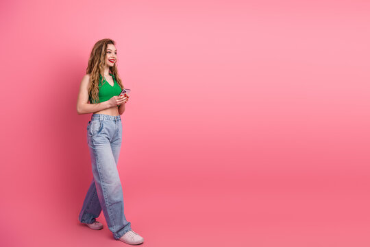 Young fashionable woman with a phone in hand against a pink background posing confidently in trendy casual wear - Powered by Adobe
