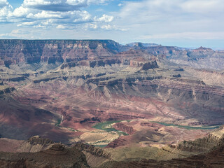 Expansive view of the Grand Canyon showcasing dramatic layered rock formations, rugged cliffs, and the Colorado River winding through the desert valley.