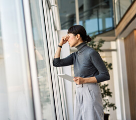Fototapeta premium Portrait of a young businesswoman standing by a window office, with headache, sick, tired or fatigue while working late . Burnout, stress and deadline concept
