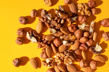 Close-up of scattered different nuts: walnut, almond, hazelnut top view on yellow background. Assorted peeled nuts, source of plant-based protein, organic healthy snack. Food background