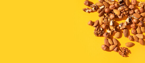Different nuts, walnut, hazelnut, almond and green leaves on yellow background flat lay top view. Mix of tasty healthy nuts, snack, appetizer. Food background. Sunlight with long shadows