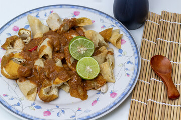 A delicious Indonesian dish of siomay served with peanut sauce and lime slices, presented on a decorative plate with a bamboo mat and wooden spoon